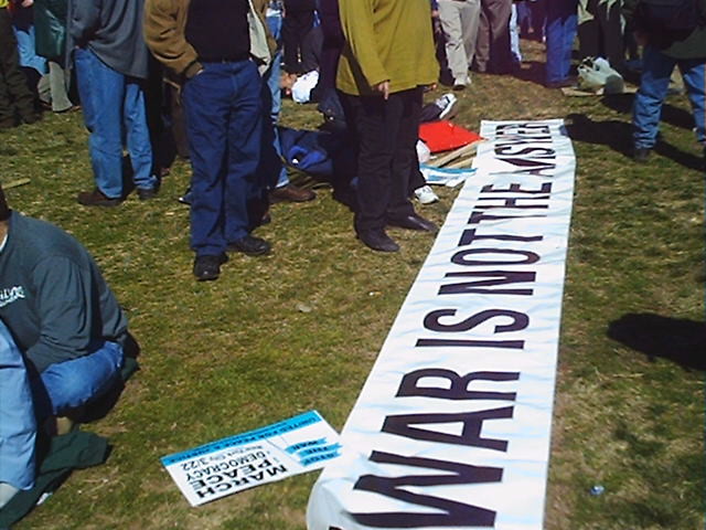 Banner draped along the ground while the protesters listen to the presenters on the stage at the rally.